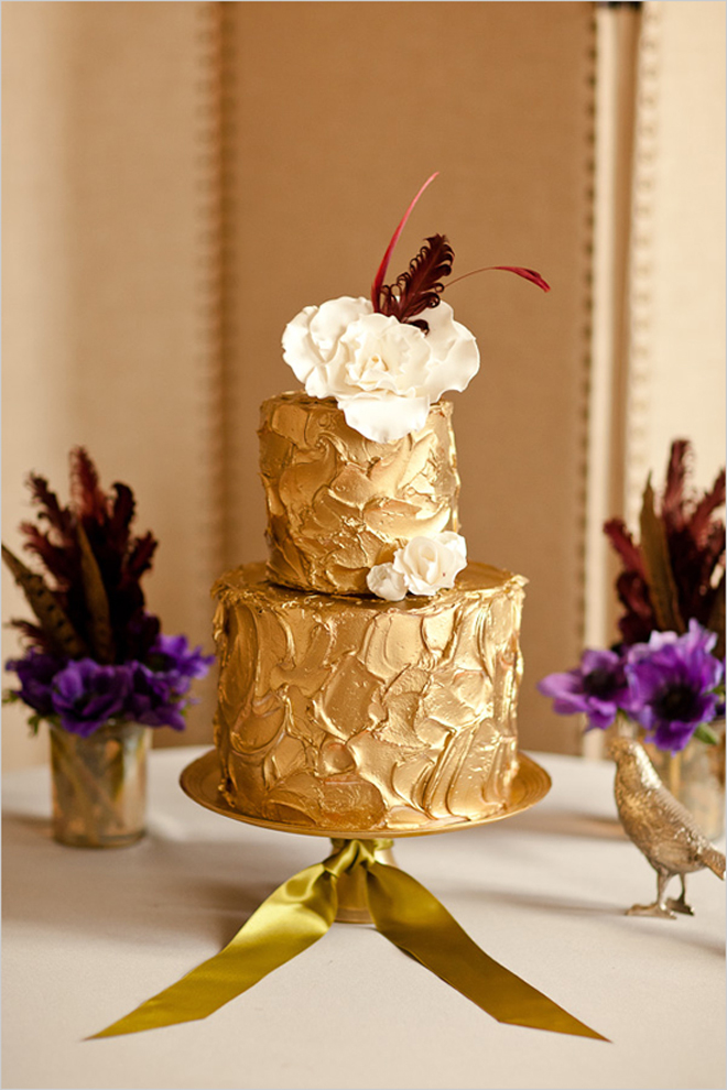 a gold textural wedding cake with sugar blooms and feathers on top for a chic and non typical wedding dessert table