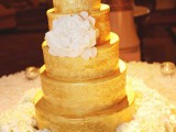 a multi-tier gold wedding cake with patterns and with a large sugar bloom for a very refined wedding