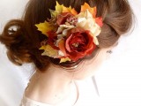 a catchy updo with a large braid and a messy low bun, with a bold faux bloom and leaves to give the bride a more fall-like look