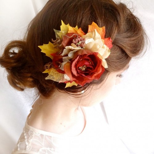 a catchy updo with a large braid and a messy low bun, with a bold faux bloom and leaves to give the bride a more fall-like look