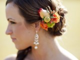 a wedding side half updo with a twisted low bun and accented with an orange bloom and greenery headpiece