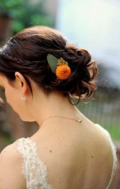 a wedding updo with a braided halo and waves in a low bun, with a bright orange bloom accent is cool for the fall