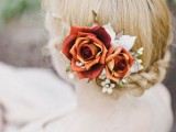 a lovely wedding updo with a braid and a bold floral accent with burgundy roses and some leaves for a delicate fall bride’s or bridesmaid’s look