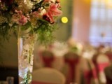 a tall pink and white floral centerpiece with greenery in a tall clear vase for a spring wedding