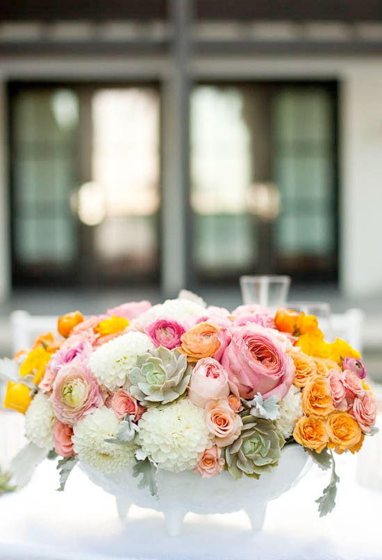 a white pot on legs with orange, pink and blush blooms and pale succulents is a chic and lush idea
