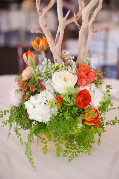 a bright spring wedding centerpiece of red and white blooms, greenery and branches for more texture