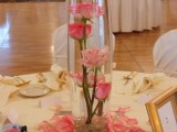 a pink wedding centerpiece of pink roses in a vase and on a mirror plus petals all around