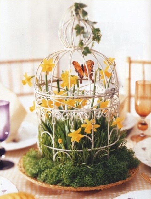 a whimsy cage spring wedding centerpiece with yellow blooms, grass, butterflies and a cage