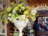 a green and peachy floral centerpiece in a tall urn is great for a spring wedding