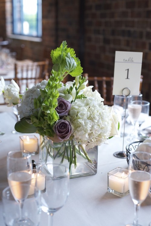 a white floral wedding centerpiece with some greenery and a couple of mauve blooms that make the arrangement look cool