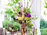 a greenery, twig and branch wedding centerpiece with a touch of purple blooms and burlap for a rustic spring wedding