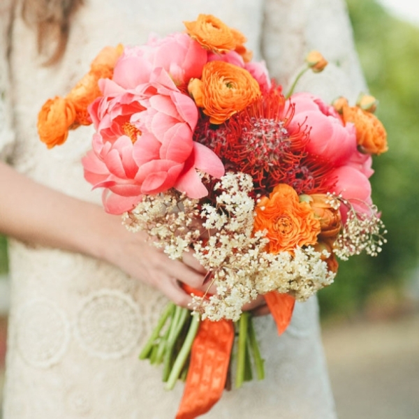 A bold wedding bouquet of orange ranunculus, pink peonies, white blooms and pincushion proteas is a lovely idea for summer