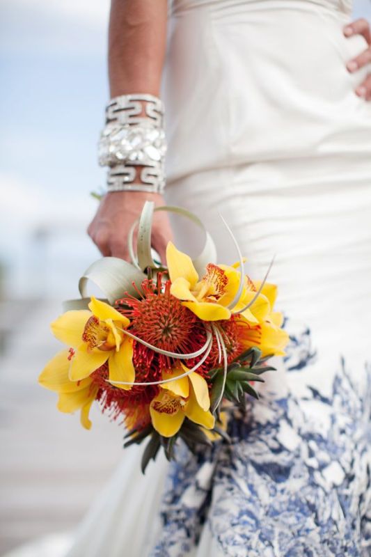 A tropical wedding bouquet of pincushion proteas, yellow orchids, succulents and twigs is a cool and fun idea