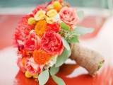 a colorful wedding bouquet of red peony roses, orange blooms, yellow roses, billy balls and pincushion proteas