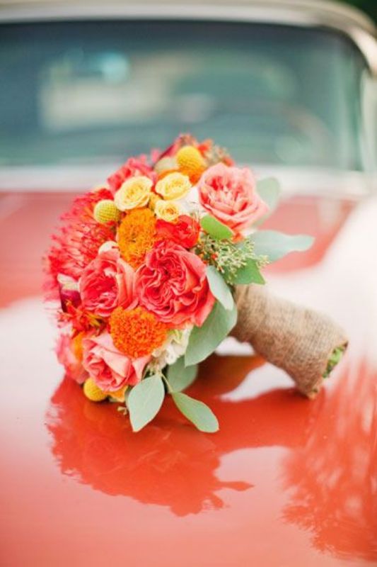 A colorful wedding bouquet of red peony roses, orange blooms, yellow roses, billy balls and pincushion proteas