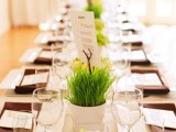 a modern spring wedding tablescape with brown napkins, neutral plates and linens, potted wheatgrass and pretty menus