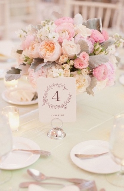 a refined spring wedding table setting with a pastel pink floral centerpiece, candles, a green tablecloth and silver cutlery