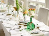 an exquisite spring wedding tablescape with neutral linens and a green runner, bold and white blooms and greenery, silver cutlery and vintage books