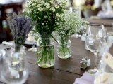 a neutral spring wedding tablescape with simple blooms in jars, neutral plates and lilac napkins plus candles