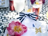 a vivacious spring wedding table with a printed tablecloth, plates and ribbons, bright pink blooms and white square chargers