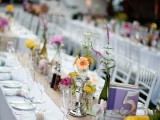 a vintage spring wedding tablescape with a burlap runner, white napkins with colorful rings, bold blooms in silver vases and stacks of books