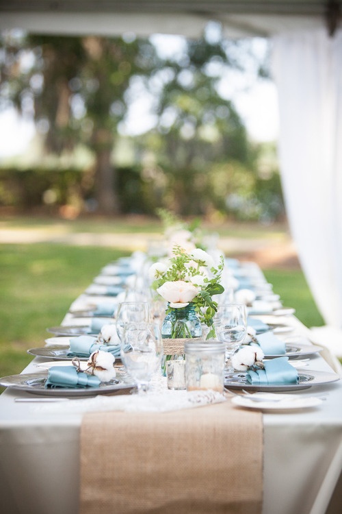 a pastel spring wedding table with a burlap runner and touches of blue - napkins and jars, with neutral blooms, greenery and cotton