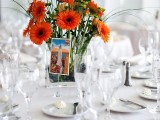 a spring wedding tablescape in white, with a super bold orange flroal centerpiece and photos and all white everything