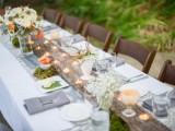 a woodland spring wedding tablescape with a log with candles, neutral and orange blooms, moss and grey napkins
