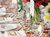 a bold wedding tablescape with a floral runner, bold red and neutral blooms, candles and neutral porcelain is fun and bright