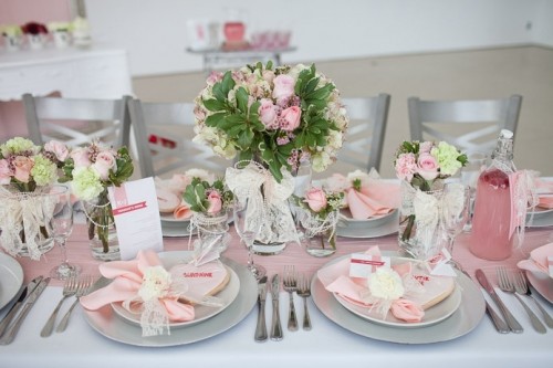 a romantic pink spring wedding table with a pink runner, pink blooms and napkins, silver and white plates, pink lemonade and silver cutlery