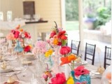 a bright wedding tablescape with neutral linens, bold blooms in white and colorful vases and gilded fruits on each place setting