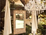 a unique wedding backdrop idea with fabric, a mirror, blooms and a crystal chandelier