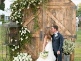 old barn doors with greenery and white blooms, a cage and a bucket with blooms is a chic wedding backdrop