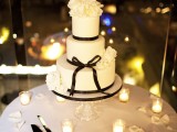 a white wedding cake decorated with black ribbones, bows and topped with white blooms
