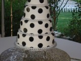 a white wedding cake decorated with oversized black polak dots and a shiny and sparkling topper