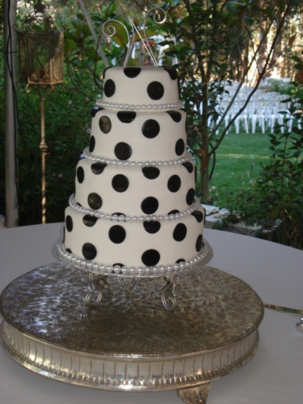 A white wedding cake decorated with oversized black polak dots and a shiny and sparkling topper