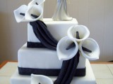 a white square wedding cake decorated with black ribbons, sugar callas and a topper