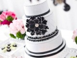 a black and white wedding cake with patterns and silver decor plus an oversized sugar bloom