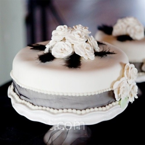 a white wedding cake with grey ribbon, sugar blooms and black feathers is a bold and cool idea