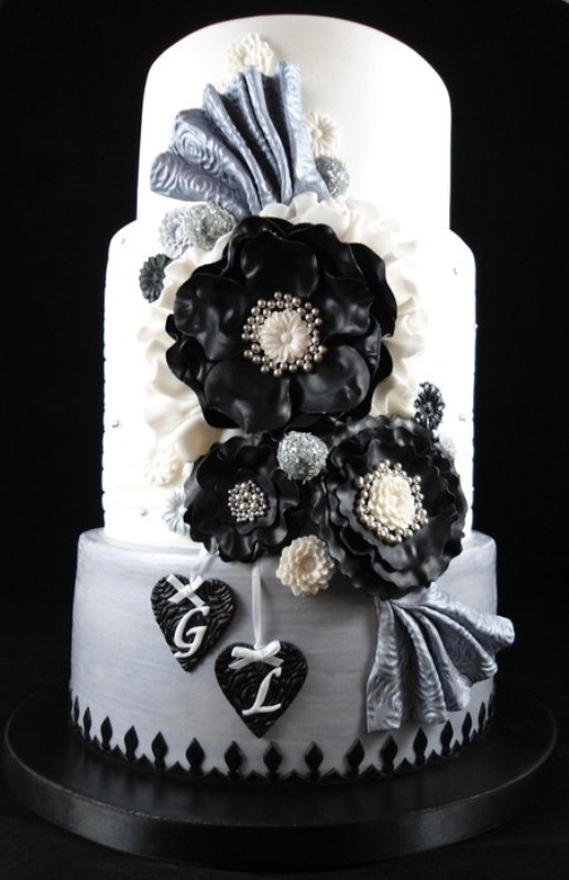 A white wedding cake decorated with black and grey sugar blooms, bows, hearts and beads