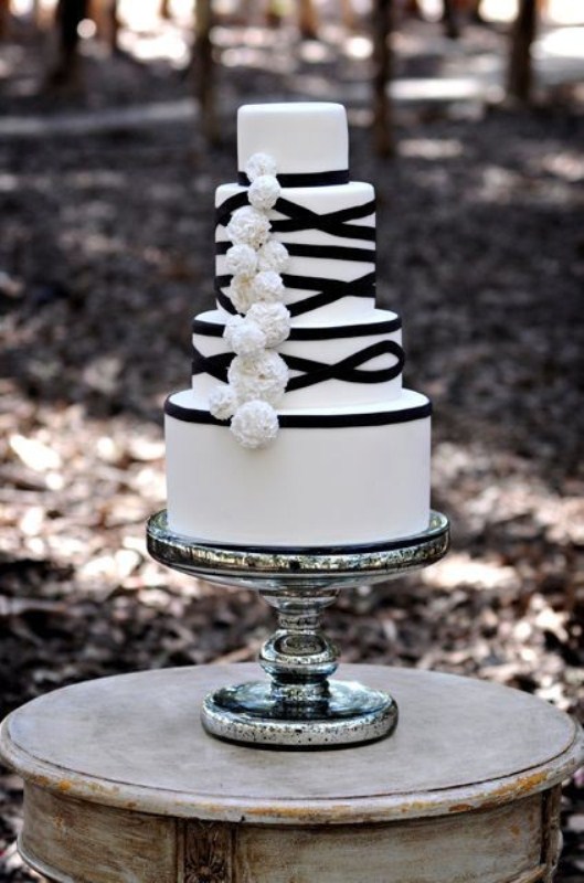 A white wedding cake decorated with black ribbons and white fluffies for a cool and bold look
