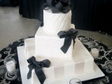 a white square wedding cake with various patterns on each tier, black ribbons and stripes