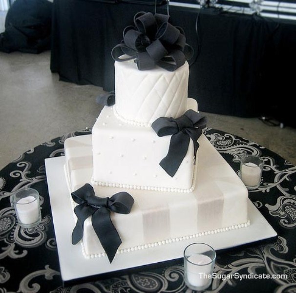 A white square wedding cake with various patterns on each tier, black ribbons and stripes