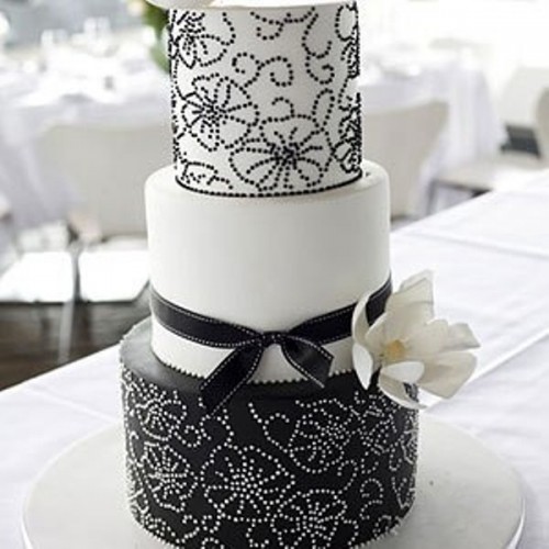 a black and white wedding cake with a solid tier and beautiful patterns plus a sugar bloom and a black ribbon bow