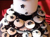 a modern white wedding cake decorated with black flowers and lots of matching cupcakes for a modern wedding