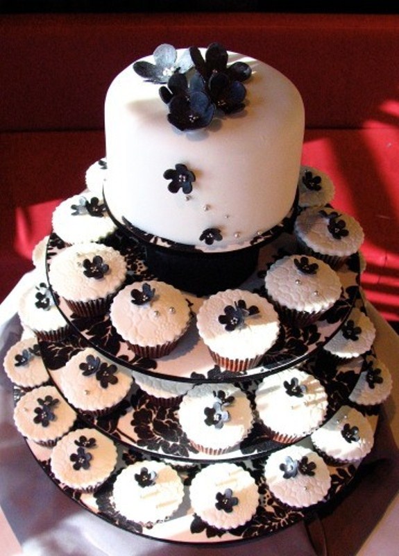 A modern white wedding cake decorated with black flowers and lots of matching cupcakes for a modern wedding