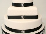 a timelessly elegant wedding cake in white decorated with black ribbons, brooches, beads and a sugar bloom on top