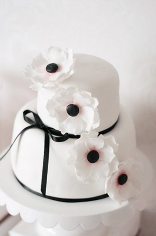 a white wedding cake spruced up with blakc ribbons and a bow plus some sugar anemones on top