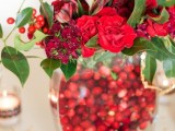 a beautiful fall or winter wedding centerpiece of a clear vase filled with cranberries and deep red blooms