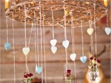 a wedding chandelier with candle-like bulbs, hearts hanging down and bottles with deep red blooms